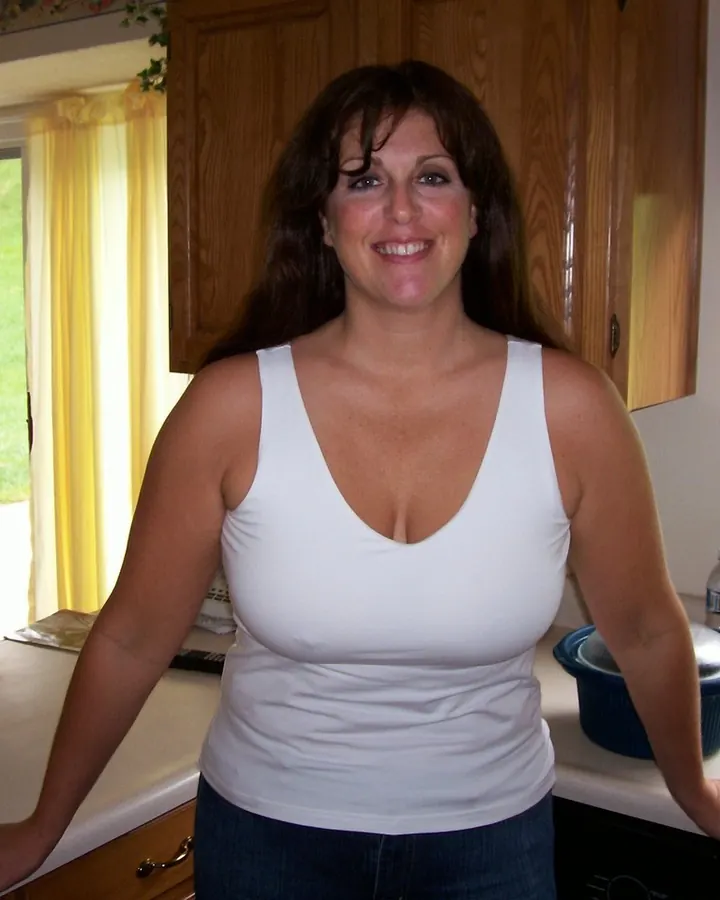 Femme souriante en débardeur blanc dans une cuisine lumineuse, cheveux bruns foncés, regard chaleureux
