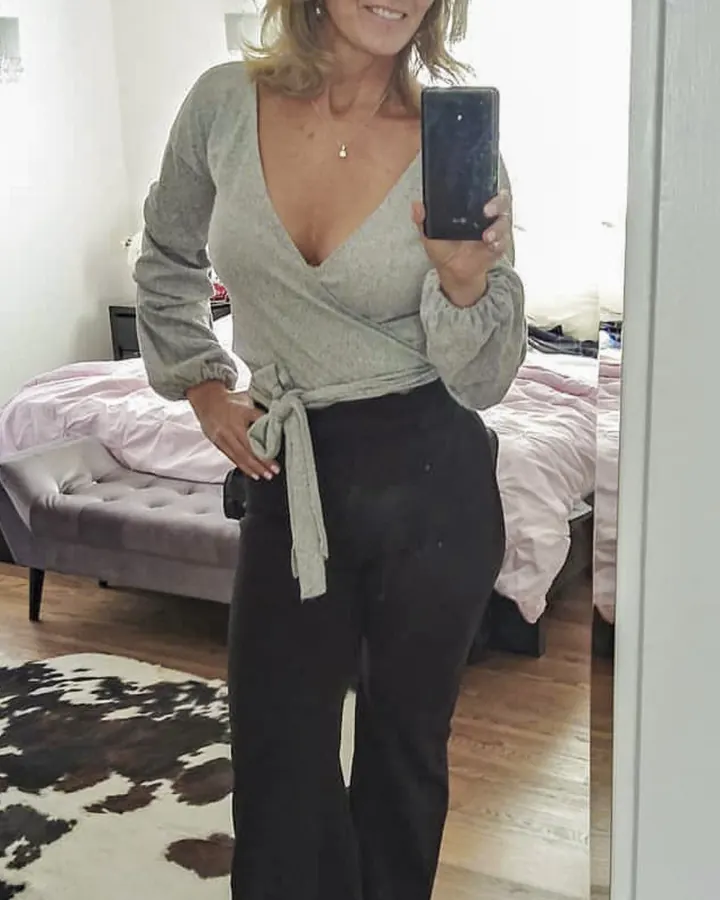 Femme blonde, portant un haut bleu foncé et tenant un verre de vin blanc, avec un chien à ses pieds.
